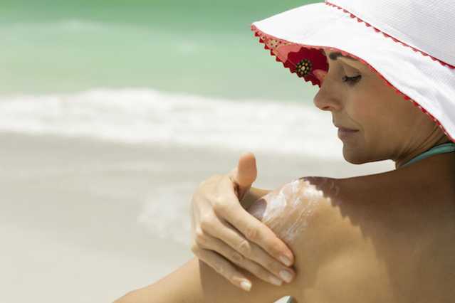 Woman applying NEUTROGENA® sunscreen to back