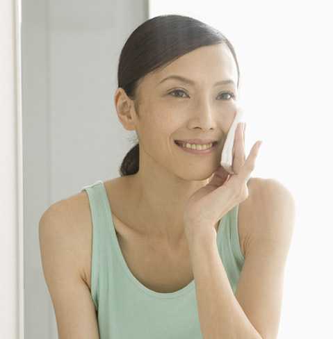 Smiling woman applying NEUTROGENA® products with a cotton pad, for anti-aging purposes.